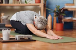 Woman with grey hair in child's pose on yoga mat